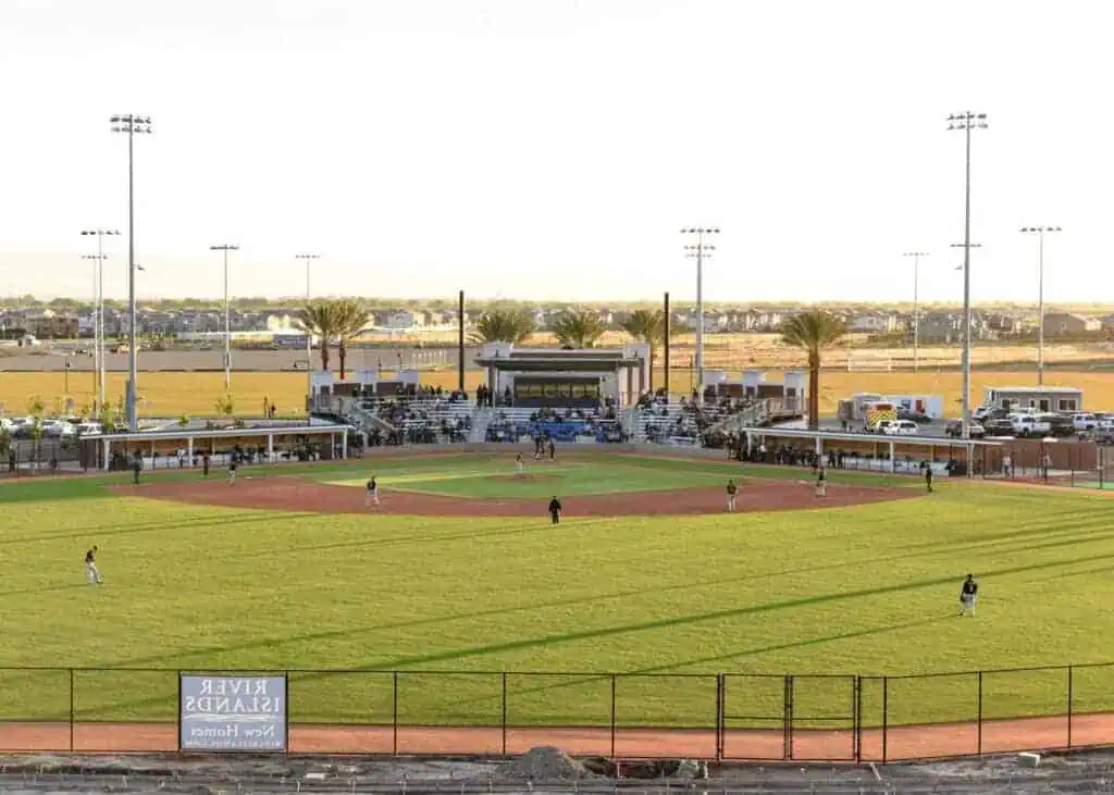 grandopen068 River Islands A baseball field with players on the infield and empty bleachers spectator stands behind home plate and palm trees in the outfield under a bright sky
