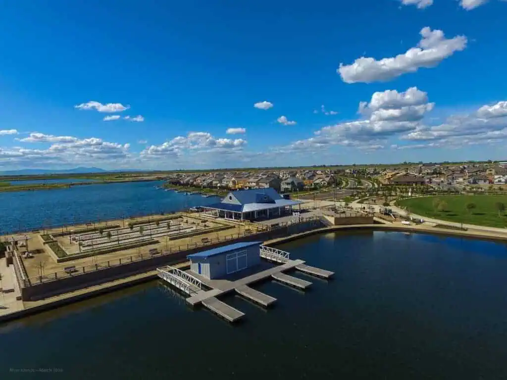 Aerial view of a waterfront park with a boathouse and docks along a large lake with houses in the distance on a sunny day