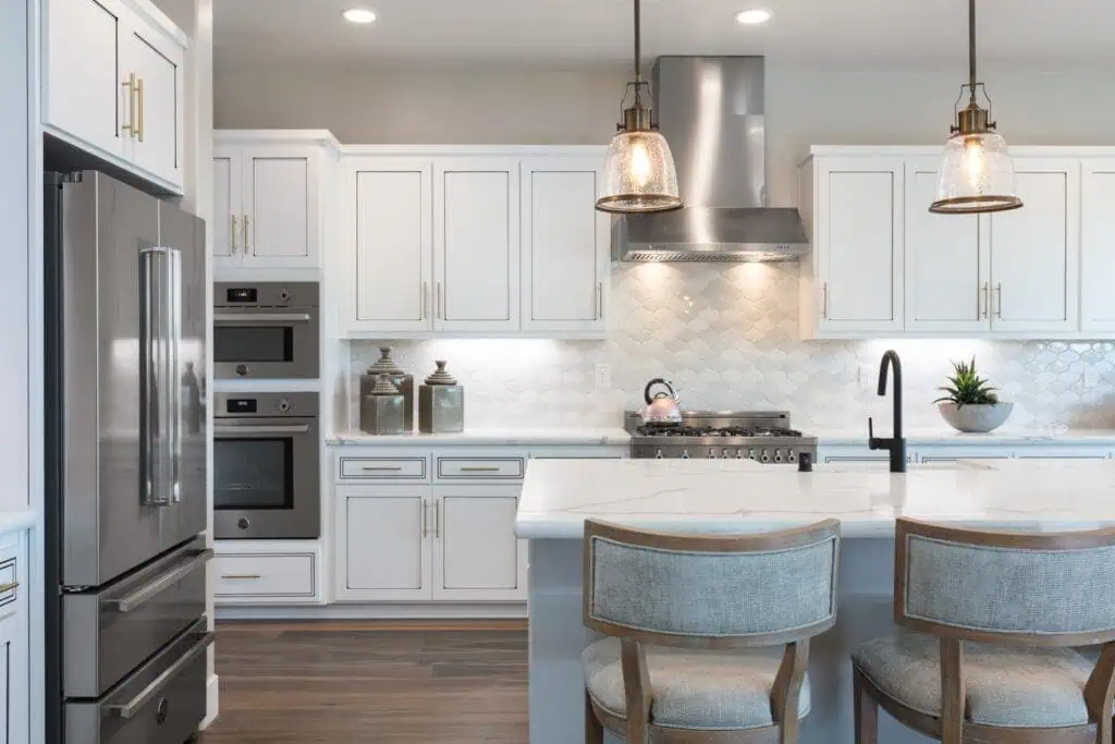 Haven and Reflections Architecture Blog 3 River Islands Bright white kitchen with a marble island stainless steel fridge double ovens and pendant lights above the island
