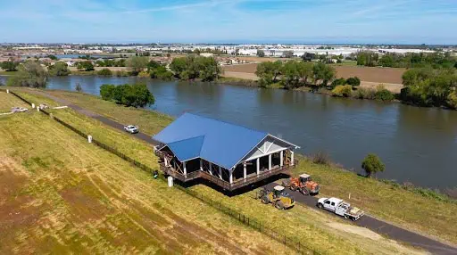 2019photo3 River Islands Blue roofed lodge by a winding river with trucks parked nearby in a grassy area