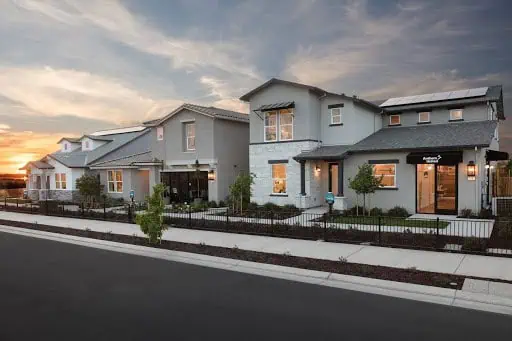 2019photo4 River Islands Row of modern two and three story townhomes with light gray siding and small front yards along a sidewalk at sunset