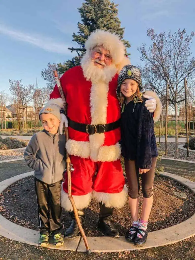 2019photo7 River Islands Santa Claus stands with two children outdoors posing for a festive photo on a sunny day in a park