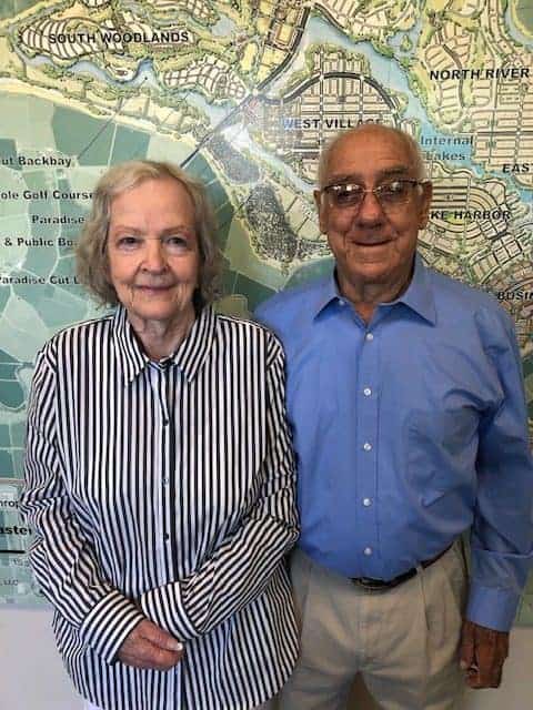 Older couple posing indoors in front of a large map wall smiling at the camera