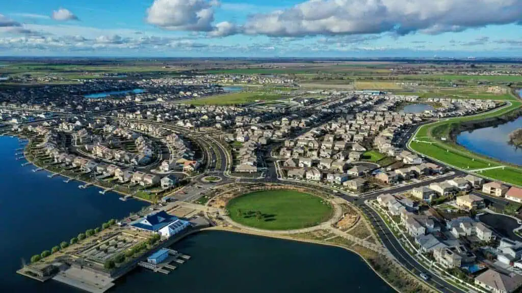 Aerial view of a lakefront suburb with curved streets, houses, and boat docks around the water's edge.