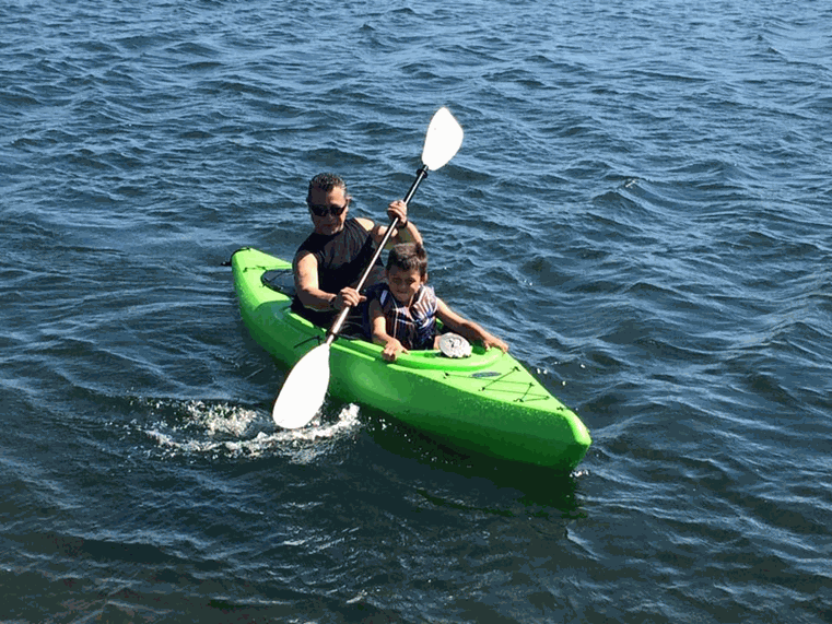 canoe River Islands Man and child paddling a bright green tandem kayak on open blue water with white paddles nearby Reached by both paddling in sync