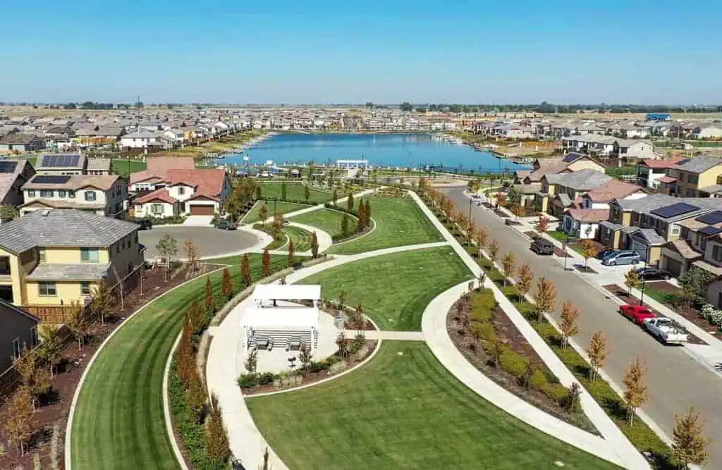 RIParkSummerHouseParkoptm River Islands Aerial view of a suburban neighborhood with winding green lawns sidewalks and a central park near a blue lake in the distance