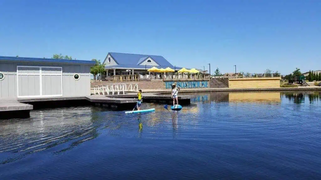 3RIBoathouse3geo River Islands two people paddle boarding on a blue lake in front of a boathouse
