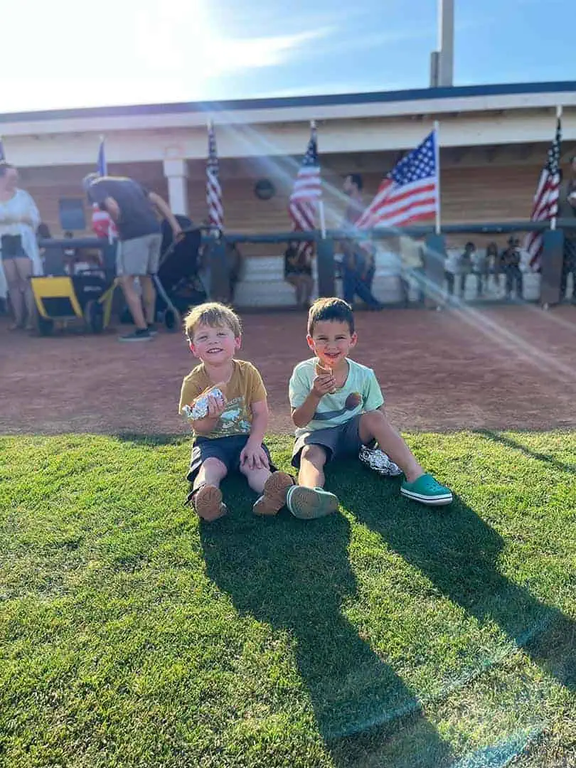 RINNOBlogPhoto3 River Islands Two young boys sit on the grass eating hot dogs at an outdoor event with American flags in the background