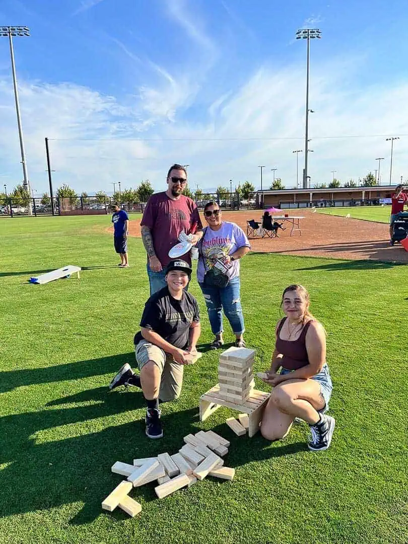 RINNOBlogPhoto6 River Islands Four people pose on a sunny field beside a giant outdoor Jenga game with wooden blocks stacked on a small bench