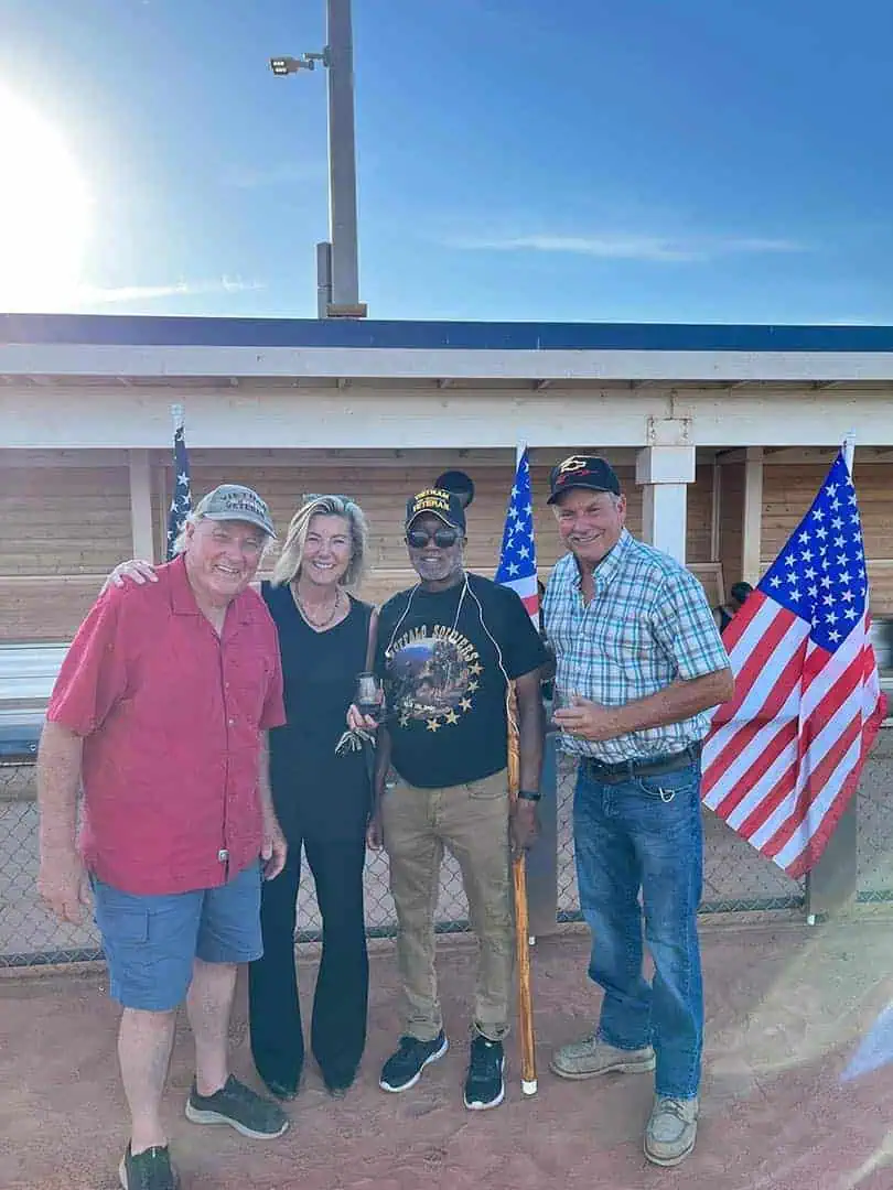 RINNOBlogPhoto8 River Islands Four adults stand together outside a wooden building with US flags smiling at the camera one man wears a Vietnam Veterans hat and holds a staff cane