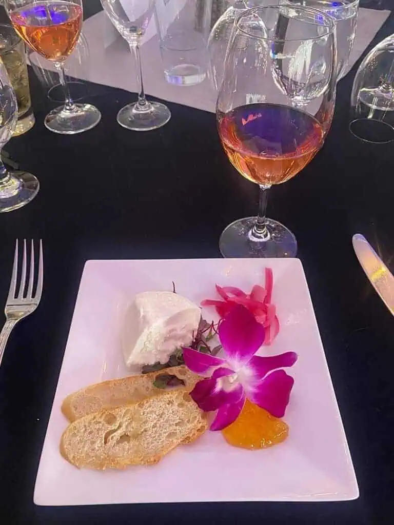2IMG8669geo River Islands Cheese plate with bread slices jam pickled onions and a purple orchid garnish on a black table with wine glasses nearby