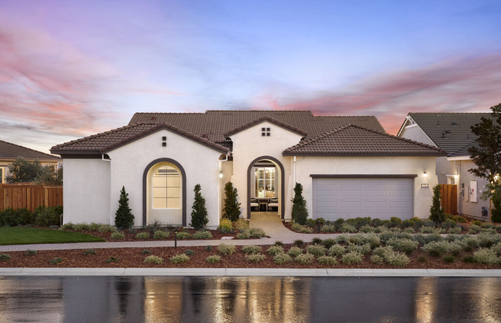 Front exterior of a modern suburban house with a tile roof arched window and a two car garage at sunset The lawn and shrubs are landscaped in front