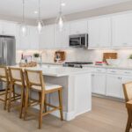 Modern kitchen in Bridgeway Plan 3501 at River Islands featuring white cabinetry, stainless steel appliances, and a central island with seating.