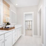 Primary bathroom in Bridgeway Plan 3501 at River Islands with dual sinks, walk-in closet, glass shower, and modern white cabinetry.