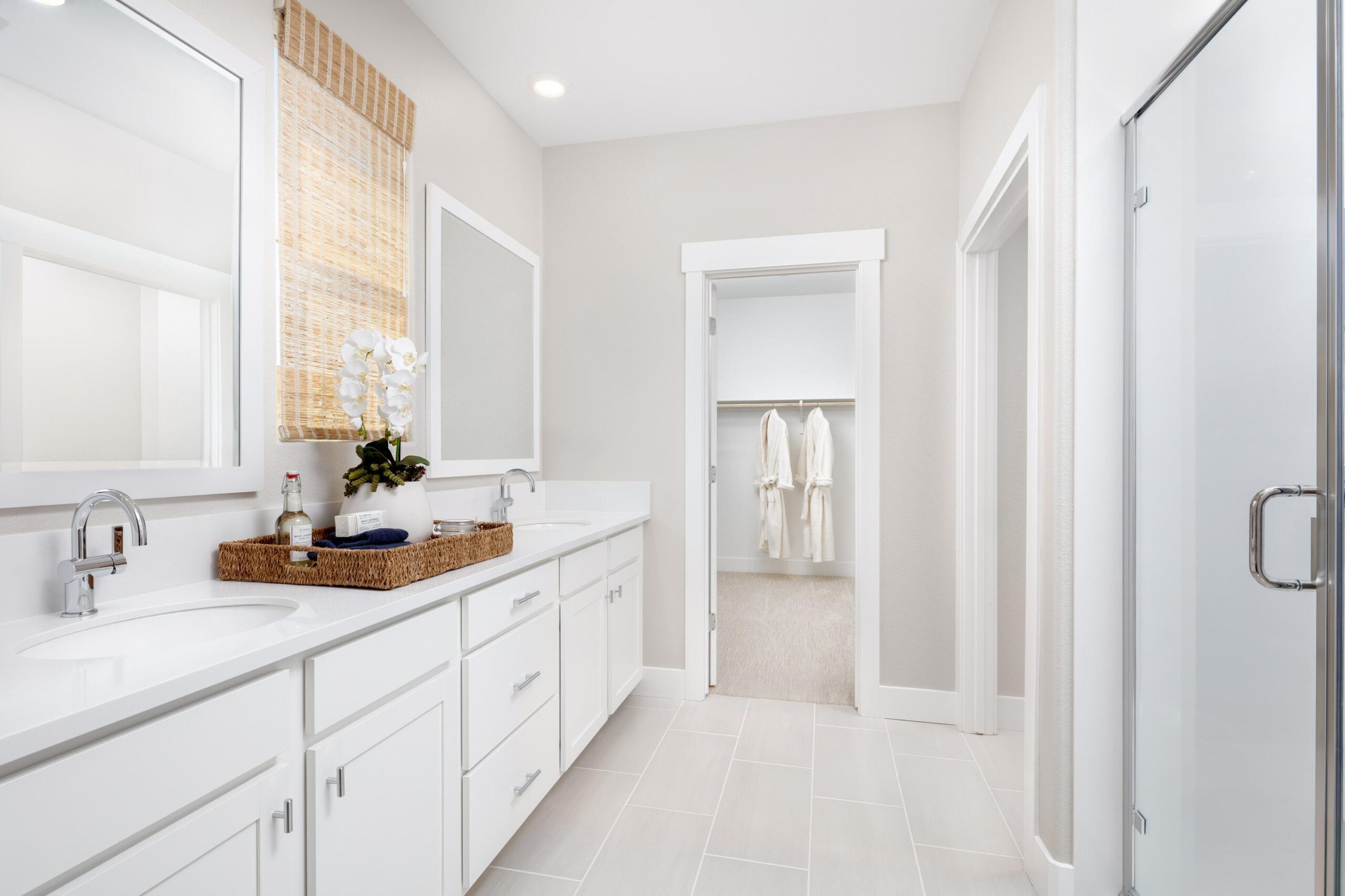 Primary bathroom in Bridgeway Plan 3501 at River Islands with dual sinks, walk-in closet, glass shower, and modern white cabinetry.