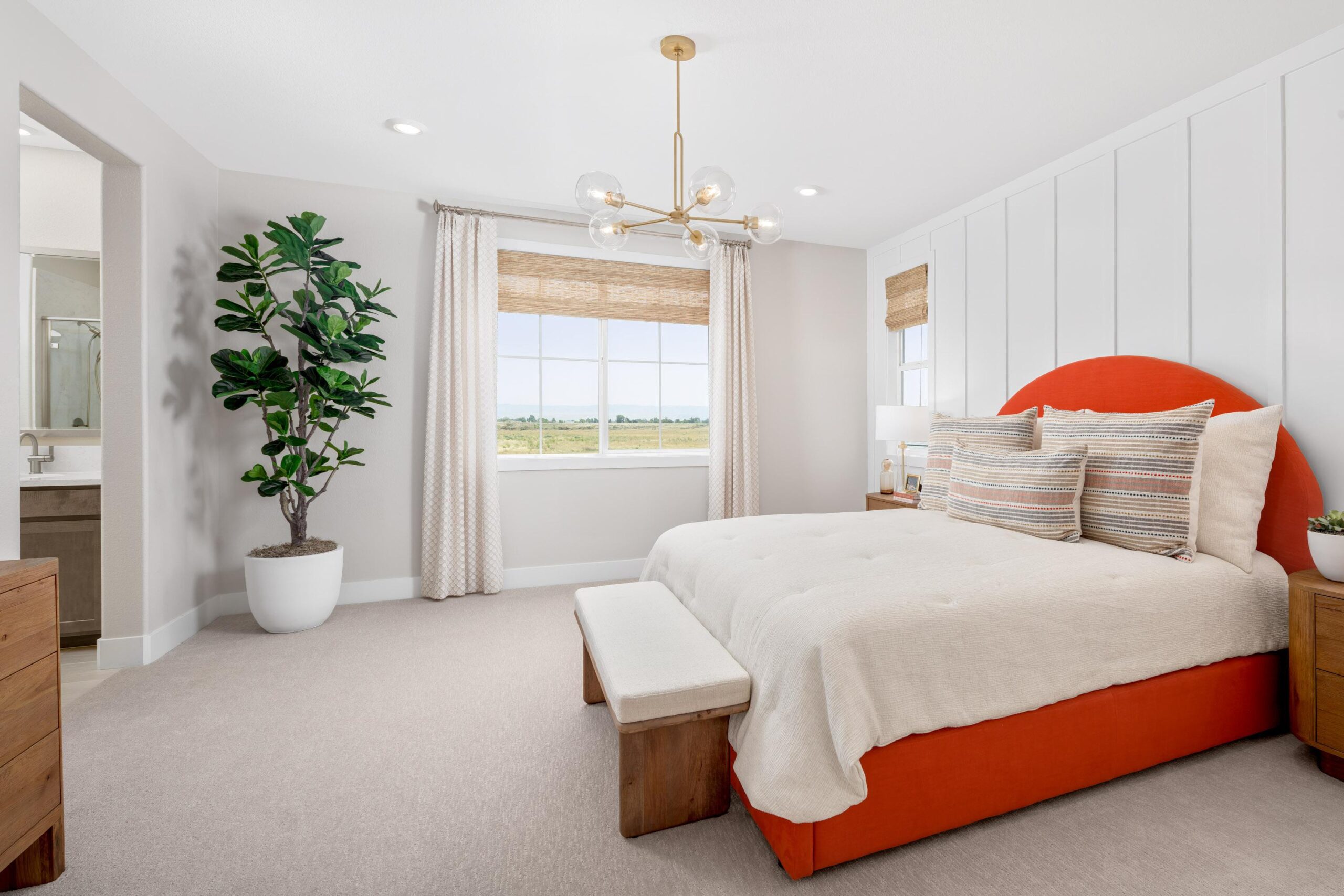 Spacious primary bedroom in Bridgeway Plan 3502 with modern chandelier, large windows, and upholstered orange bed.