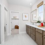 Elegant primary bathroom in Bridgeway Plan 3502 with dual-sink vanity, framed mirrors, and walk-in closet access.