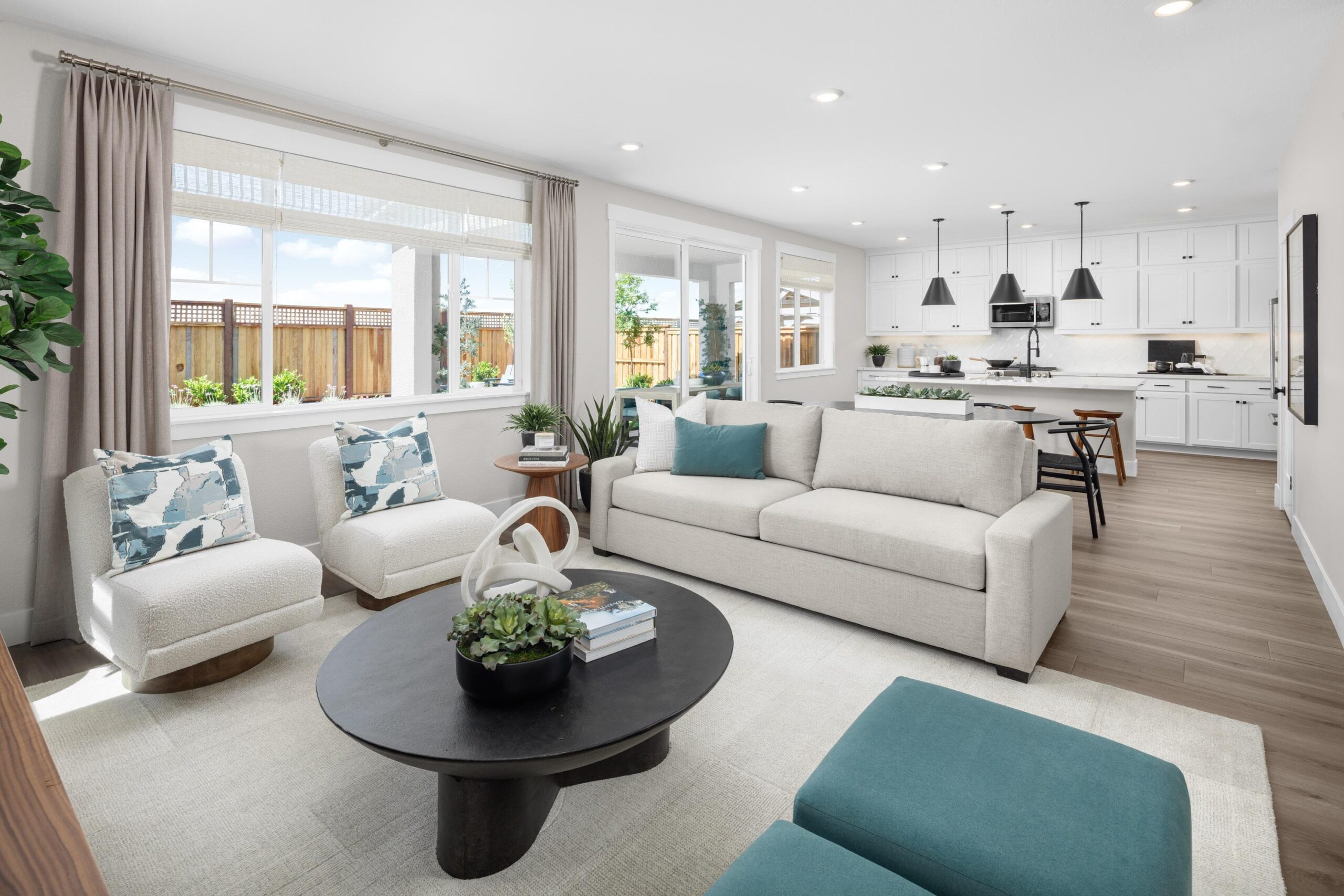 Open-concept living room and kitchen in Bridgeway Plan 3503 at River Islands featuring modern white cabinetry, black pendant lighting, and spacious seating.