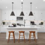 Contemporary kitchen in Bridgeway Plan 3503 showcasing white cabinets, large center island with bar seating, and stainless steel appliances.