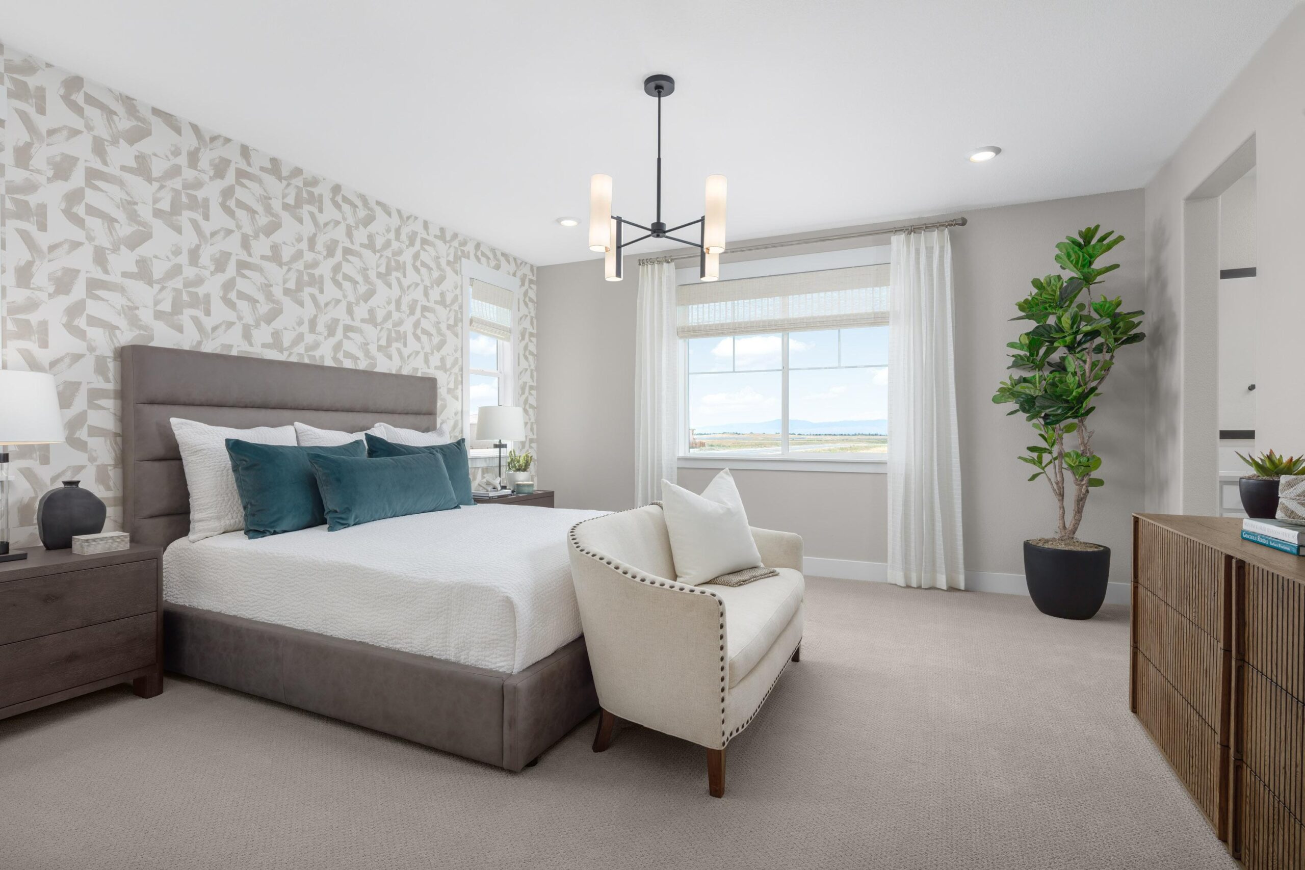 Elegant primary bedroom in Bridgeway Plan 3503 with feature wallpaper accent wall, teal decor accents, and large windows with natural light.