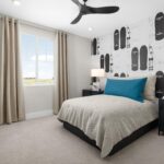Stylish secondary bedroom in Bridgeway Plan 3503 designed with skateboard accent wall, modern furnishings, and wide window views.
