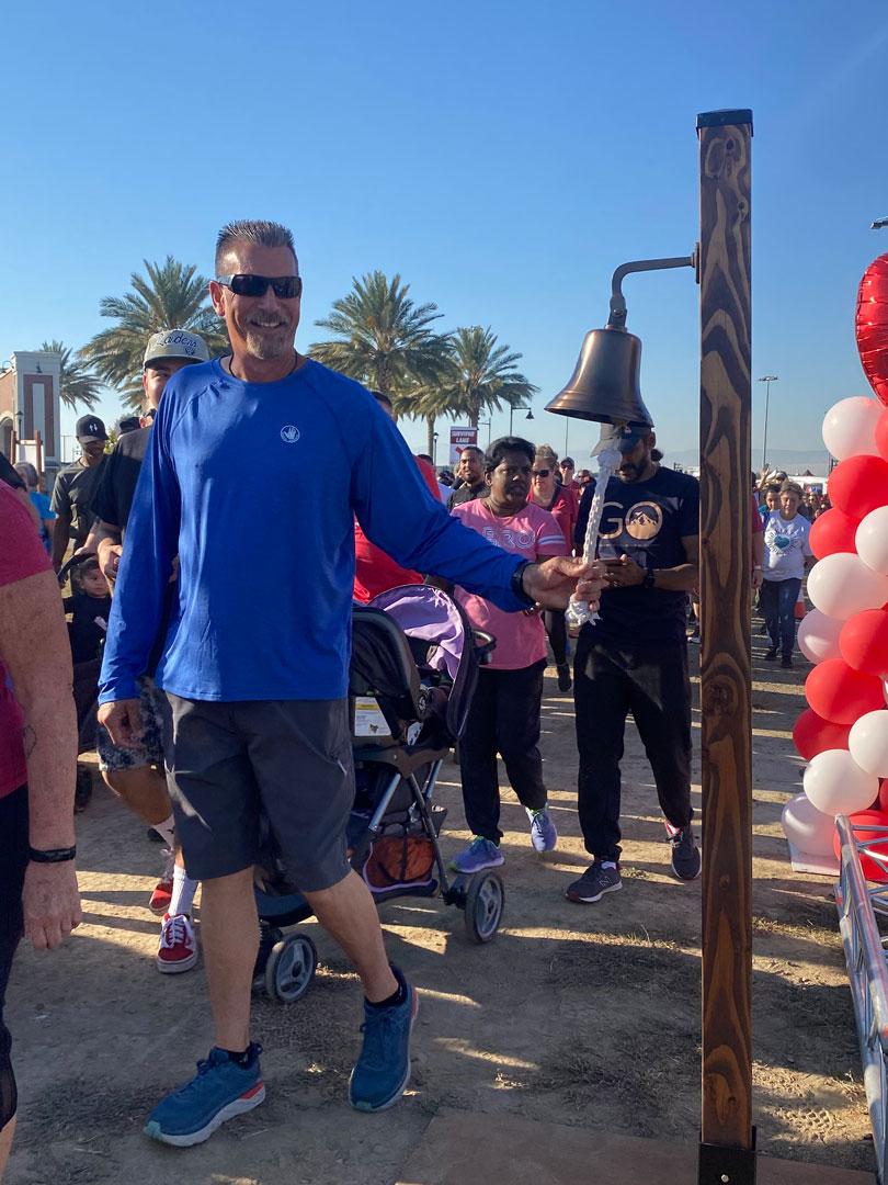 Man rings celebration bell at the 209 Heart & Stroke Walk at River Islands, surrounded by participants and balloons during the community health event.