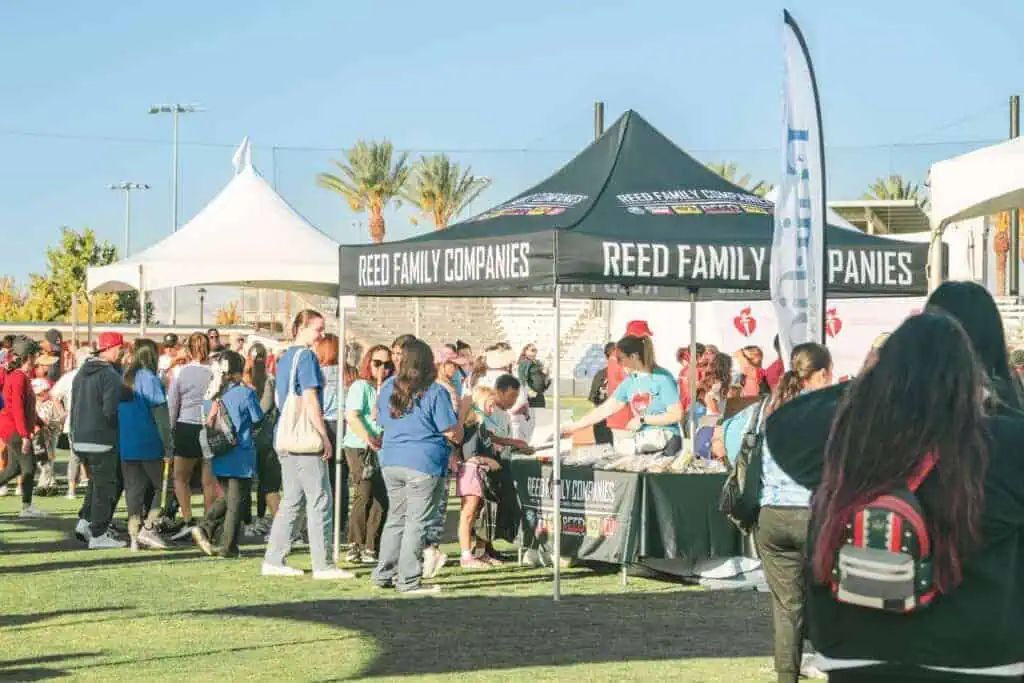 HW2512geo River Islands Crowd of people at an outdoor event gathered around a Reed Family Companies booth with banners under a canopy tent of the same name on bright day