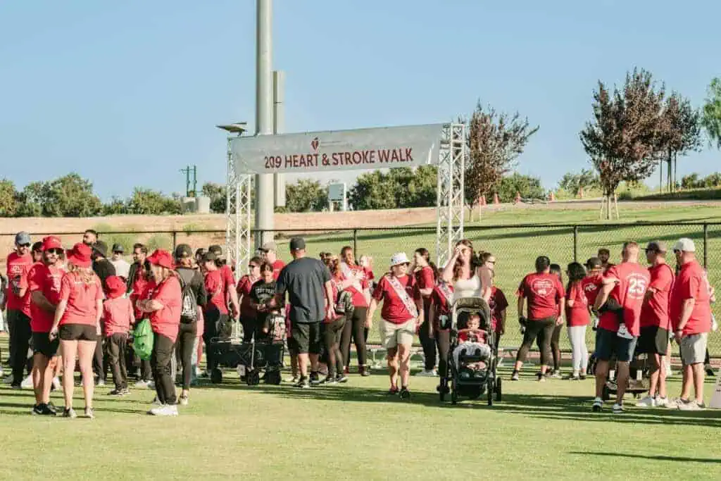 HW2535geo River Islands Group of volunteers and participants in red shirts gather under a banner that reads 209 Heart Stroke Walk on a sunny day
