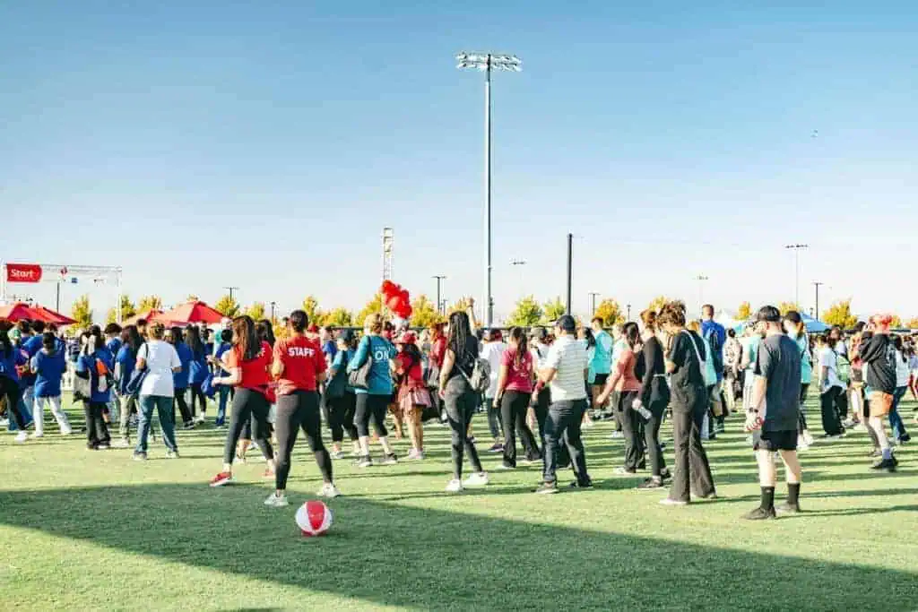 HW2544geo River Islands Crowd of people on a grassy sports field at an outdoor event some in staff shirts with a start banner visible in the background