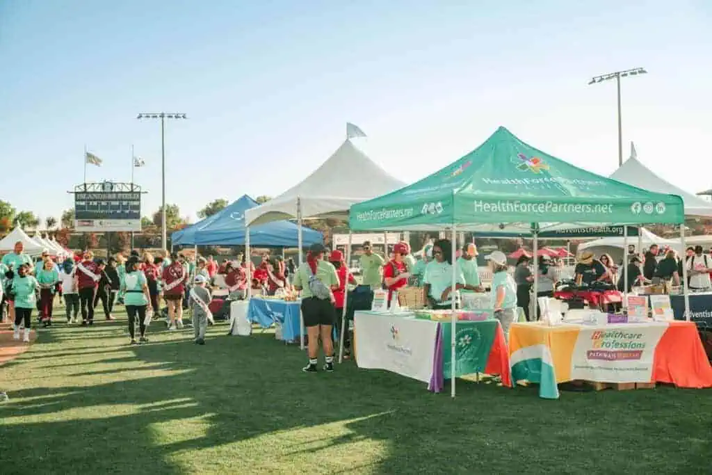 HW255geo River Islands Outdoor health fair with green HealthforcePartners tent and vendor tables on a sunny grassy field