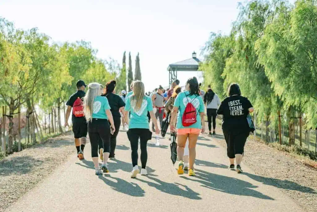 HW2565geo River Islands Group of people walking down a sunlit path lined with trees wearing matching teal shirts and backpacks