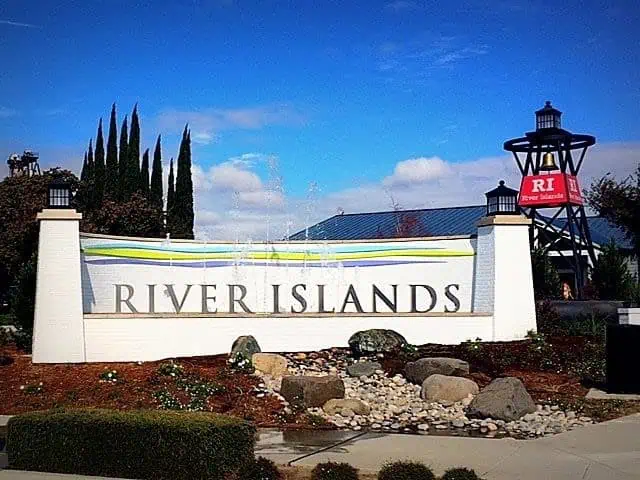 River Islands entrance sign on a white wall with a rock garden and blue sky overhead welcoming visitors