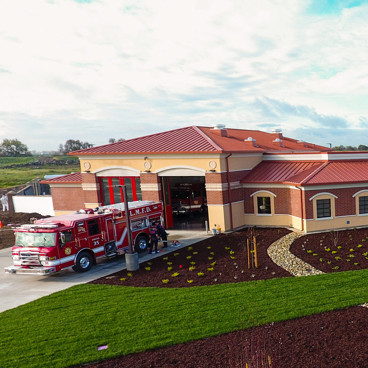 Fire engine parked at a modern red brick fire station with open bay doors