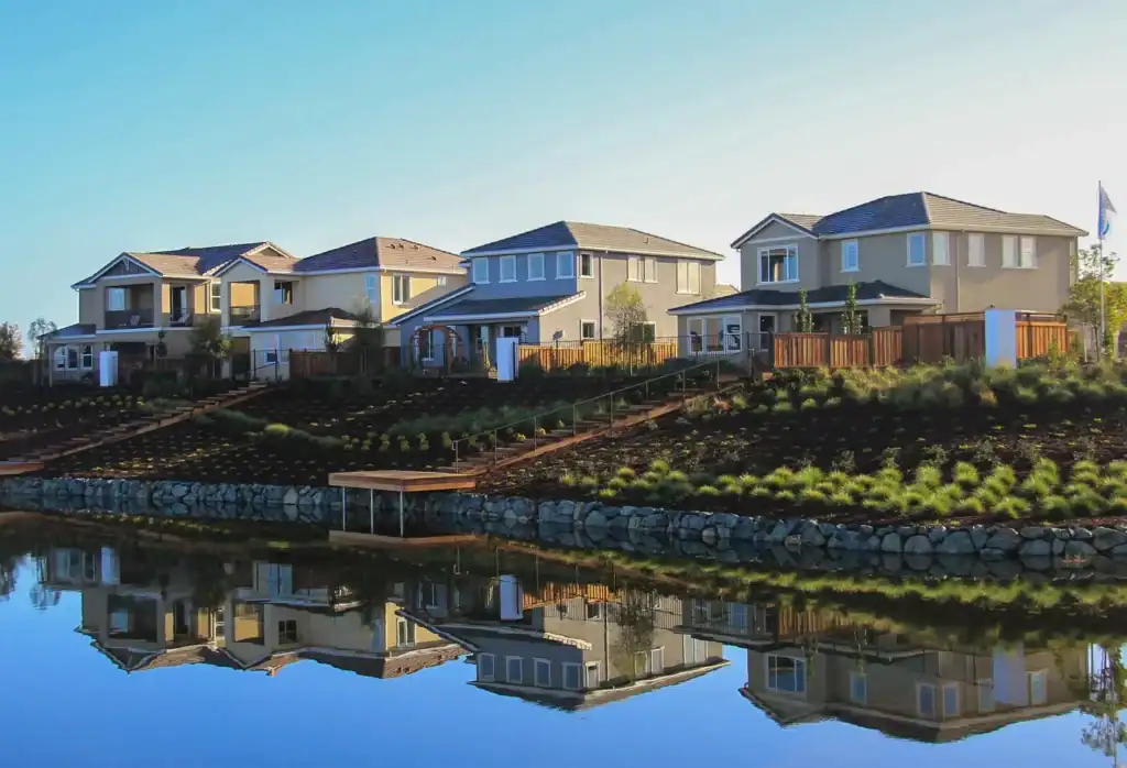 Row of modern beige two story houses on a landscaped hillside beside a calm lake reflected in the water